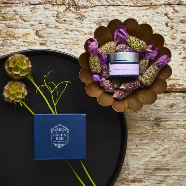 Green Bee Botanicals eye cream jar and box nestled in fresh lavender and flowers against barn wood