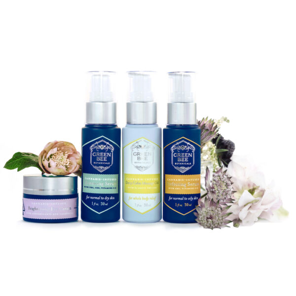 Photo of four Green Bee Botanicals cannabis-infused skincare products, including Brightening Eye Cream, Renewing Serum, Deep Calm Massage Oil and Perfecting Serum, surrounded by fresh flowers. Photo by Pamela Palma