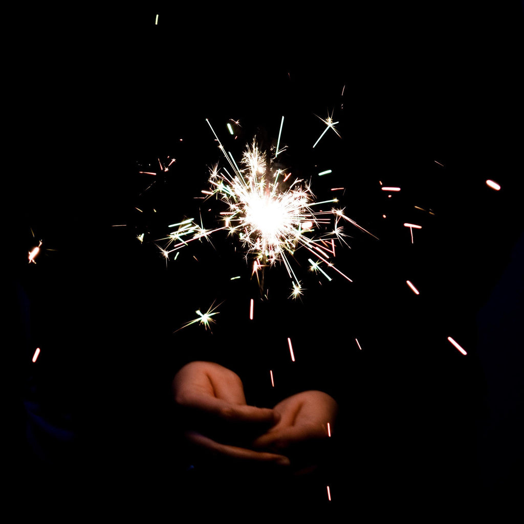 Hands holding a lit sparkler against a black background - New Year's Eve - 4th of July